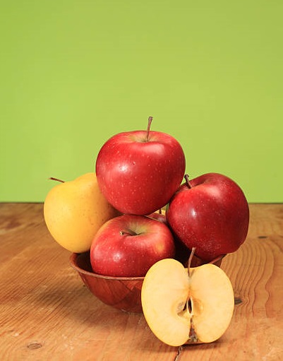 Apples in a bowl on wooden background and half apple, green background